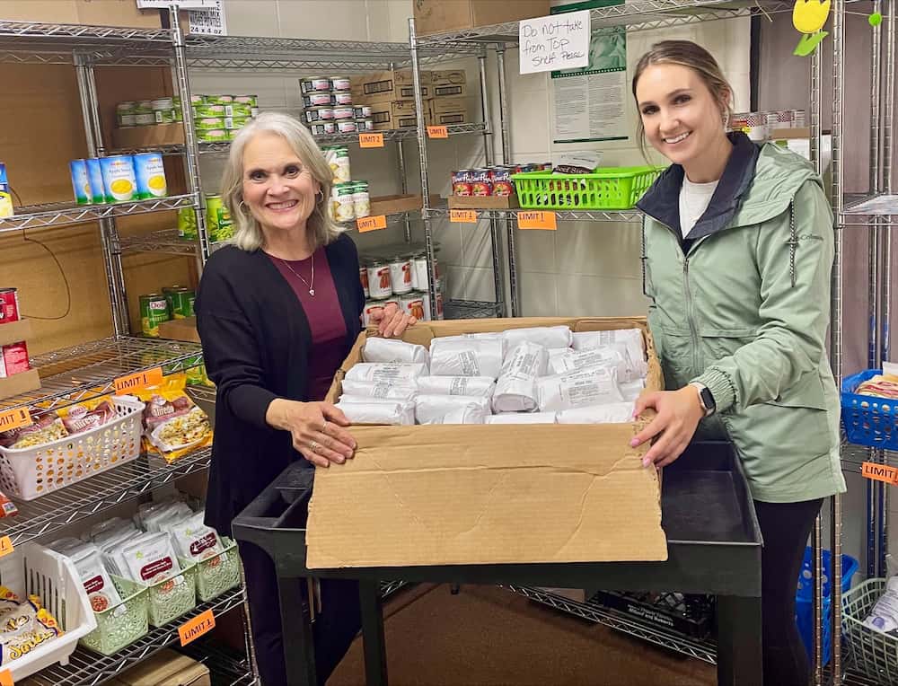 Two women standing in front of shelves holding a box of pork.
